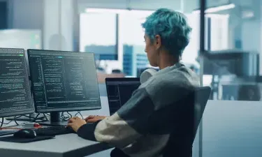 Application programmer seated in front of dual monitors in office environment coding