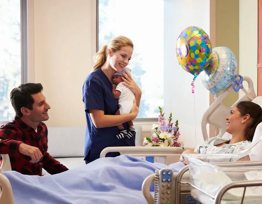 Labor and Delivery Nurse Holding Infant and Smiling with New Parents